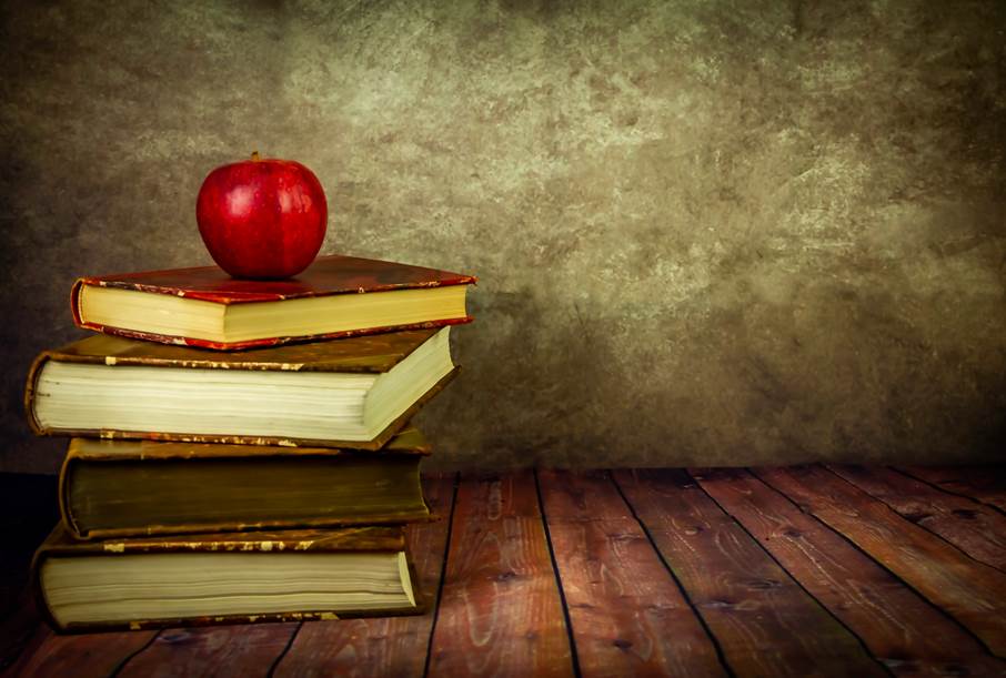 Bild på fem böcker staplade på varandra med ett rött äpple ovanpå. 