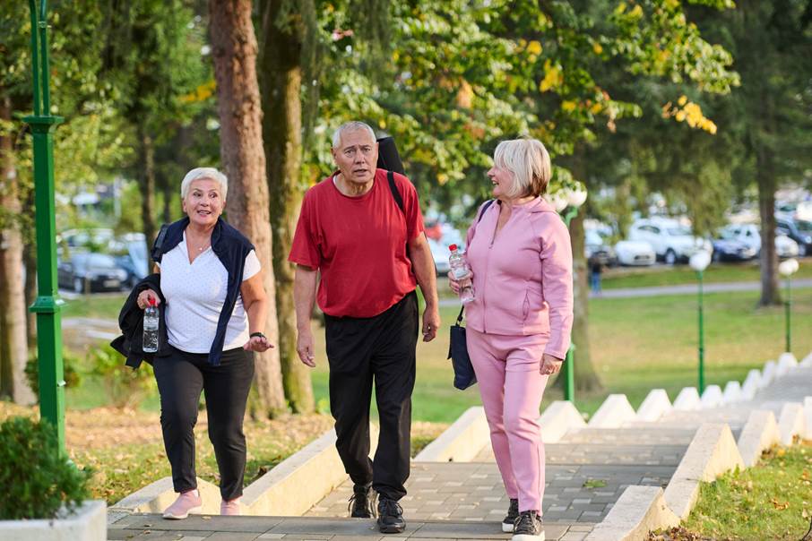 Bild på tre äldre personer i fritidskläder går och pratar på en gångbana.