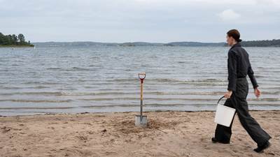 Kvinna med hink och spade på en strand.